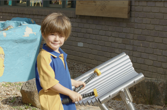A young school student playing wellbeing instruments' outdoor musical instrument "Explorer" in a school yard.