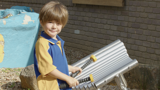 A young school student playing wellbeing instruments' outdoor musical instrument "Explorer" in a school yard.